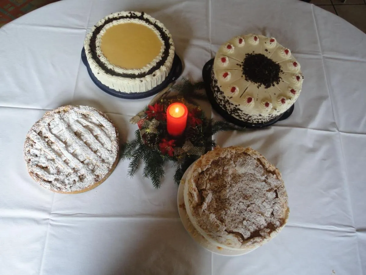 Vier hausgemachte Kuchen im Viereck angeordnet mit einer roten Kerze und Dekoration in der Mitte.