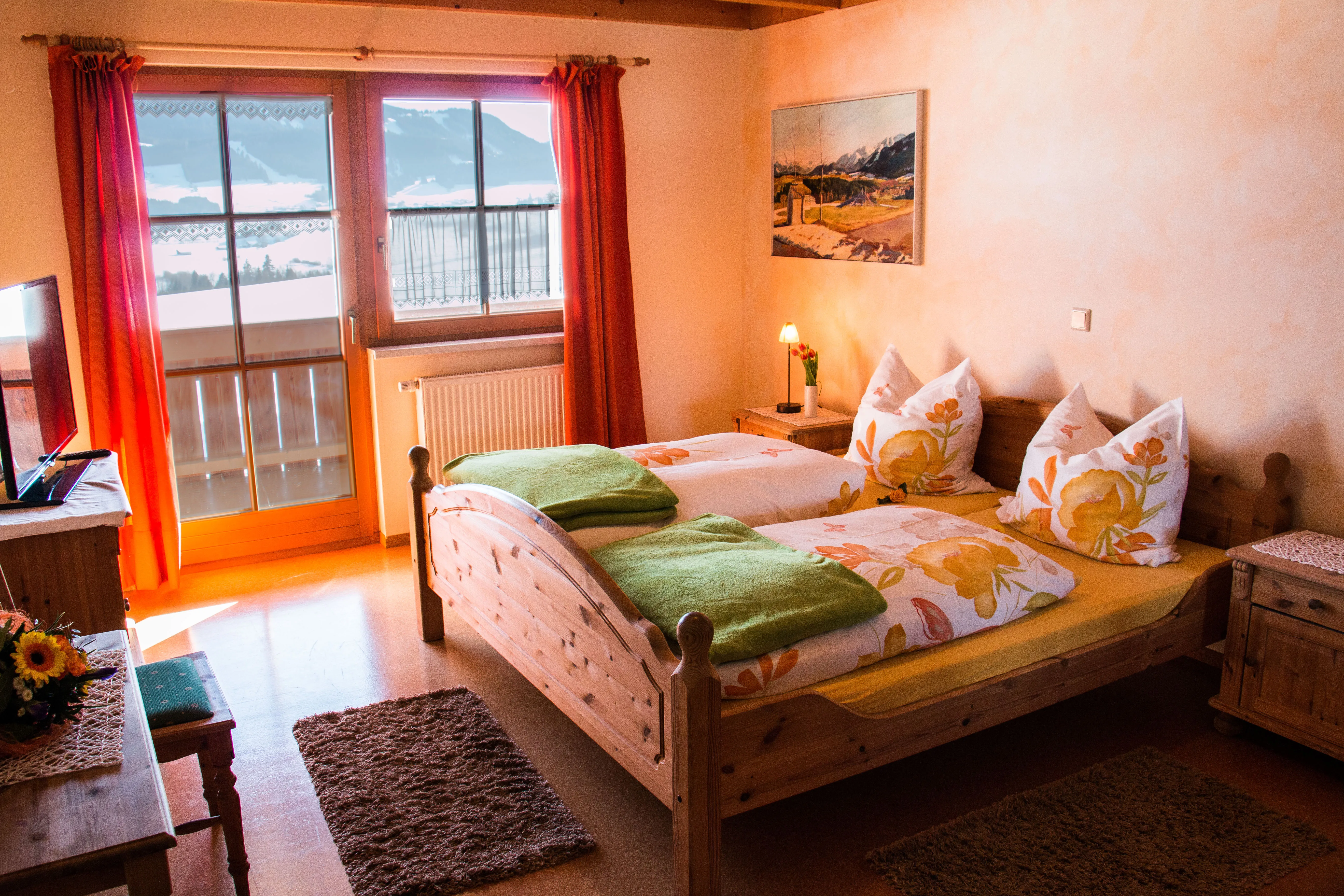 Innenansicht eines Gasthof Doppelzimmers in rot und orange gekleidet und mit smaragdgrünen Decken auf dem Bett.